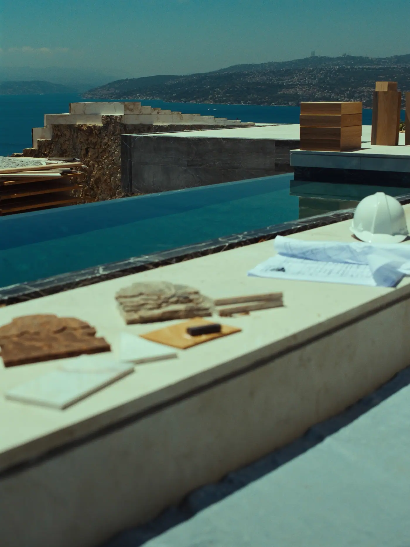 Villa şantiyesinde yeni kaplanmış havuz kenarı, mermer numuneler ve baret